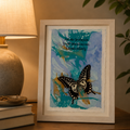 Framed artwork with a butterfly on a textured blue background next to a lamp and books.