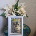 White shadow box with abstract art inside and a preserved butterfly in a blue and gold background. 