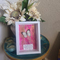 Decorative display with a framed picture of a butterfly on a pink background, surrounded by flowers and a decorative box.