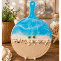Decorative cutting board with beach theme featuring blue water, sand, and shells on a wooden surface.