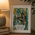 Shadowbox artwork with a butterfly design on a wooden surface next to a lamp.
