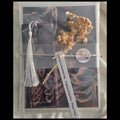 Packaged product with tassel, dried flowers, and text on a textured surface